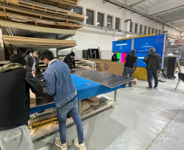 People inspecting a large blue digital display in a workshop.