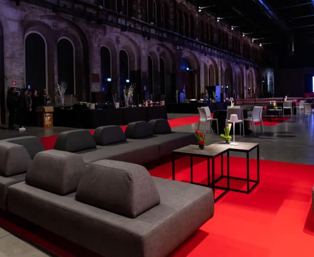 Spazio elegante per eventi con divani e tavoli in un ambiente industriale.