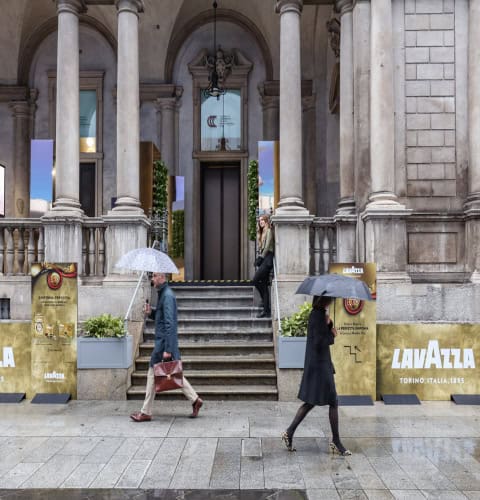Persone con ombrelli davanti a un edificio storico con colonne in pietra.