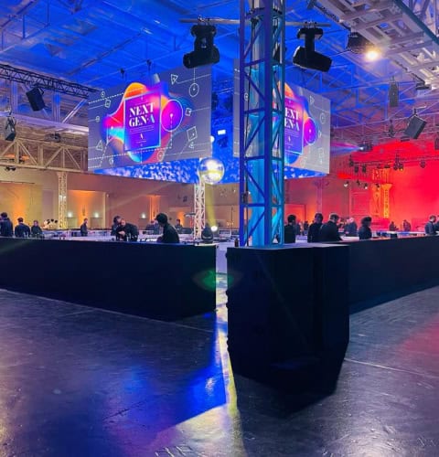 Sala eventi con luci colorate e schermi digitali per il Next Gen event.