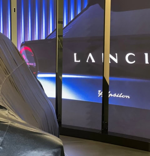 Mostra di un'auto e uno schermo digitale con logo Lancia e slogan.